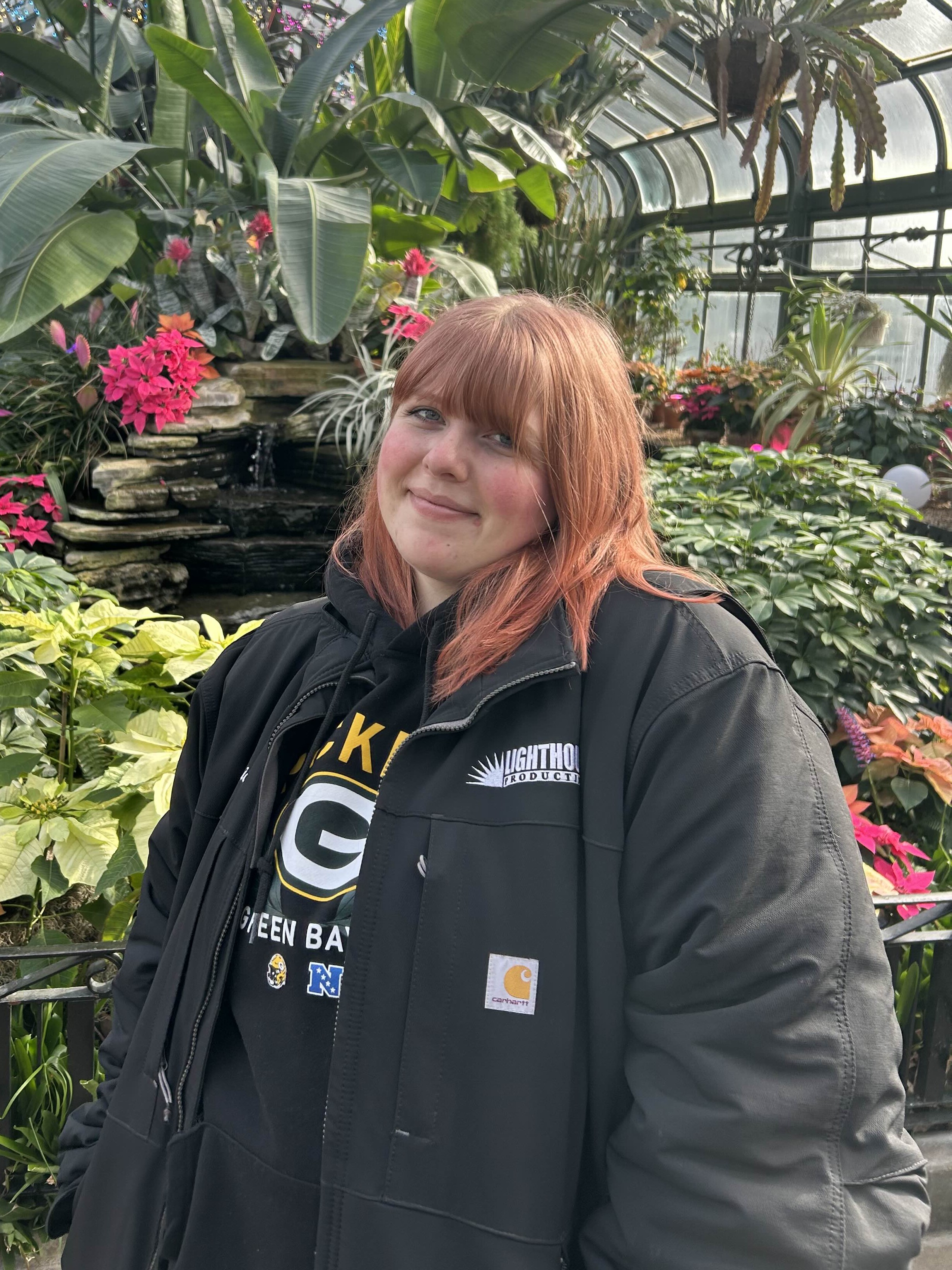 An image of Felsic wearing a winter coat and smiling
                with plants in the background.